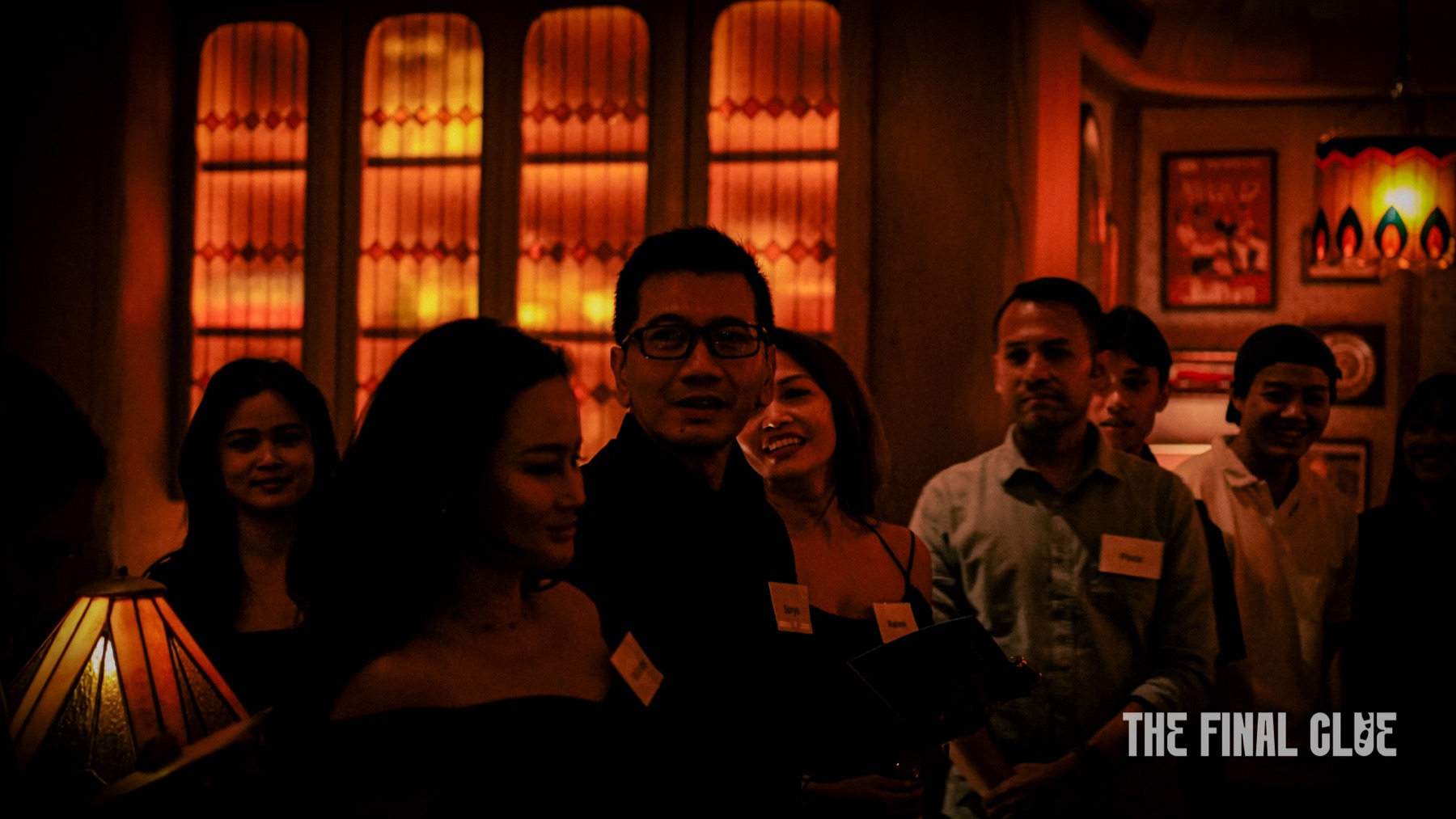 Guests gathered in a candlelit dining room at a Final Clue murder mystery dinner in Jakarta, stained glass windows glowing behind them.